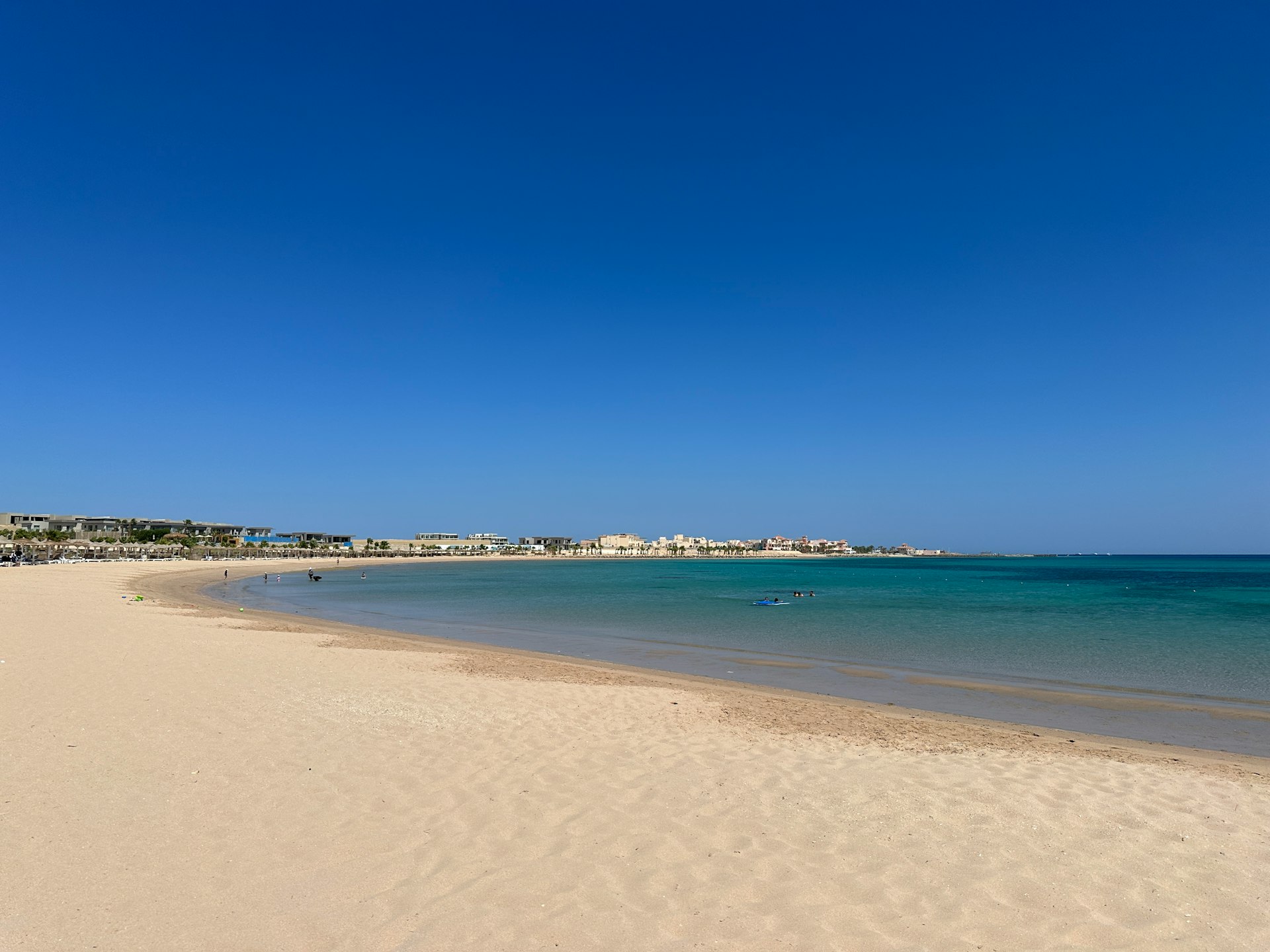 a sandy beach with clear blue water and buildings in the background